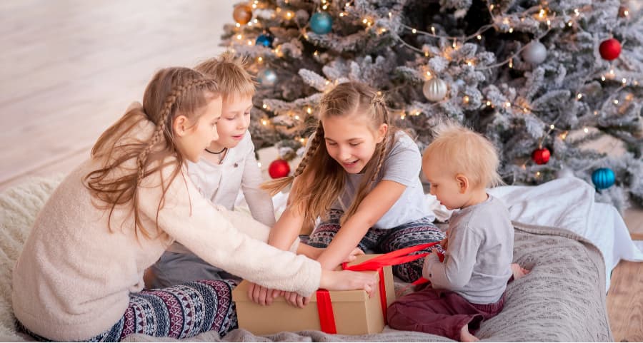 Children opening a present in the living room near a Christmas tree.